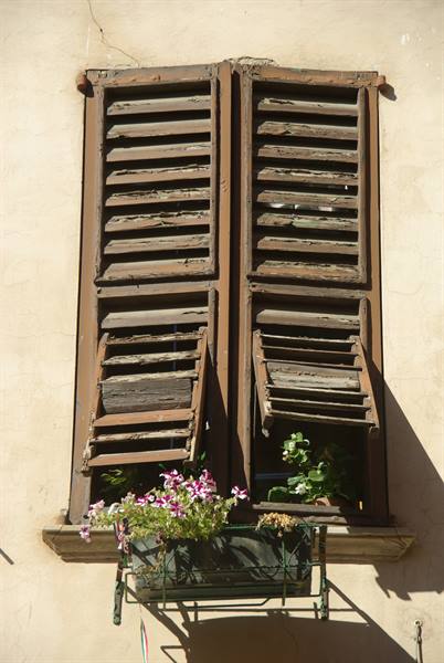 Old weathered wooden shutters, pink flowers on windowsill, sunlight