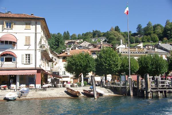 Lakeside square with boats ashore, cafés, Italian flag, houses on the hill