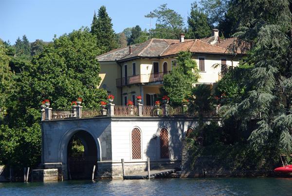 Yellow villa with stone terrace and red flowers over the lake water
