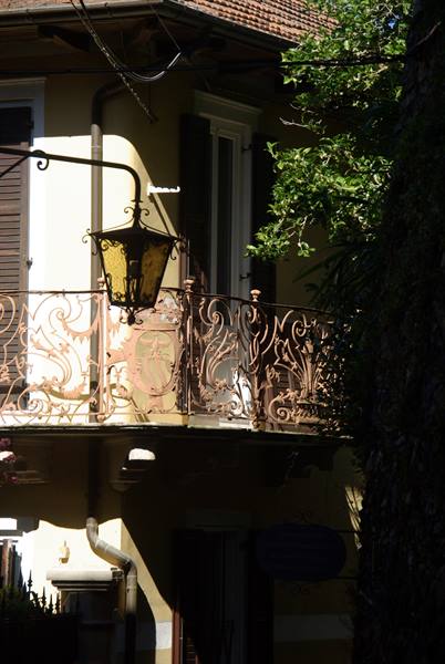 Wrought-iron lantern on ornate balcony in front of yellow house