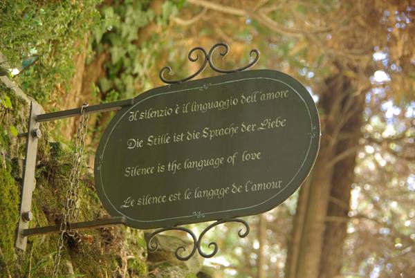 Oval metal sign with inscriptions in four languages about silence, hanging among trees