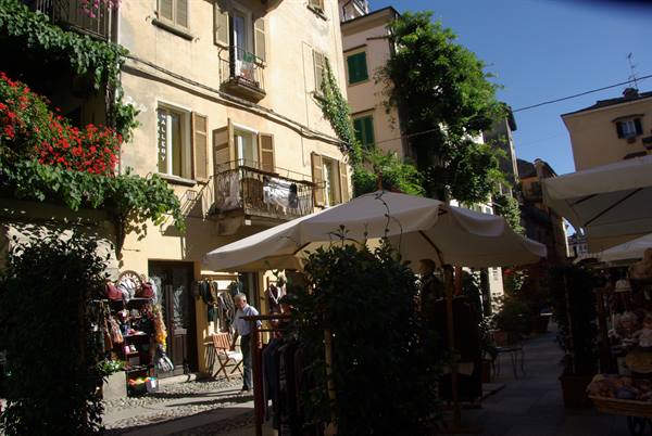 Alley with white umbrellas and flowered yellow houses, tourist among market stalls