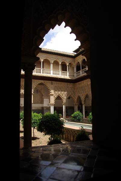 Mudéjar arches and orange trees in Seville's Alcázar courtyard, bright light