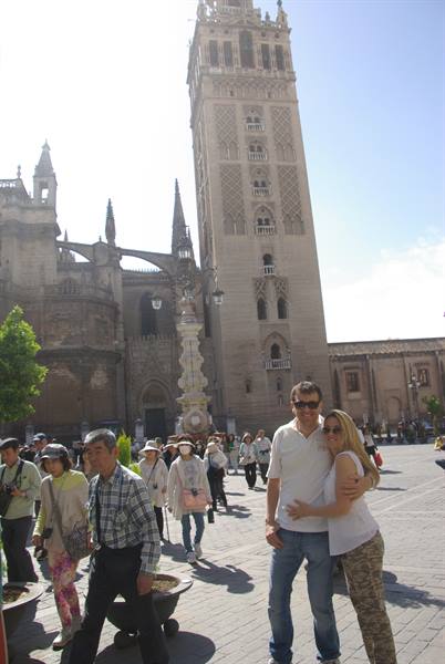 Couple posing in front of Seville's Giralda, tourists in the sunny square