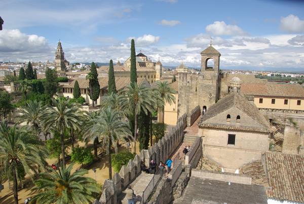 Córdoba Alcázar walls with palm trees, bell tower and tourists under sunny skies