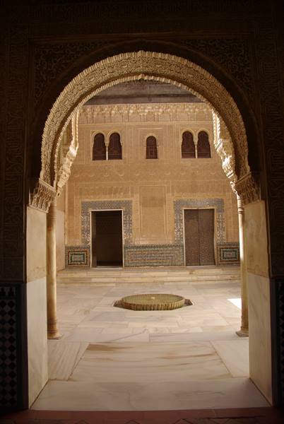 Carved Alhambra arch framing courtyard with fountain and tiles