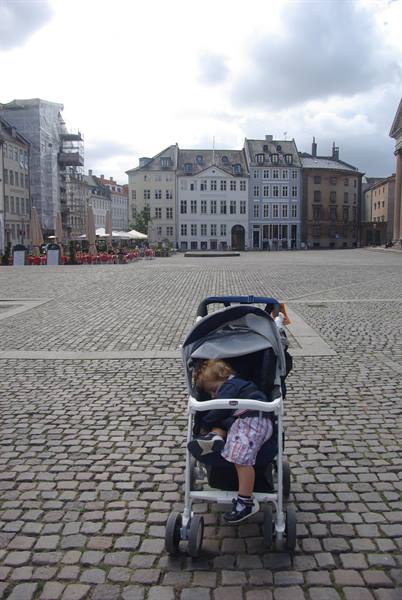 Child in a stroller on the cobblestones of a square with gray buildings