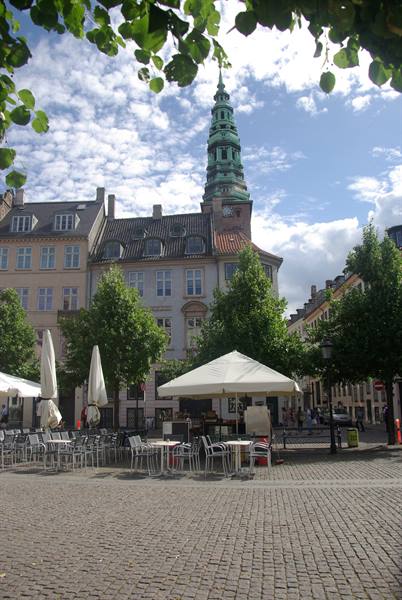 Cobblestone square with café tables and the green spire of Nikolaj, Copenhagen