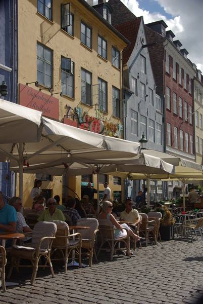 People sitting at café tables under parasols along Nyhavn's colorful houses, Copenhagen