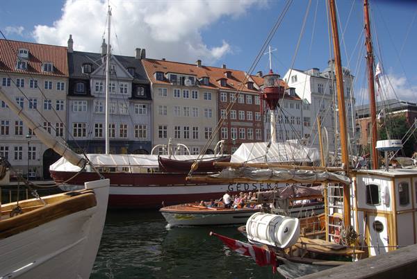 Historic boats moored at Nyhavn, Copenhagen, among colorful houses under blue sky