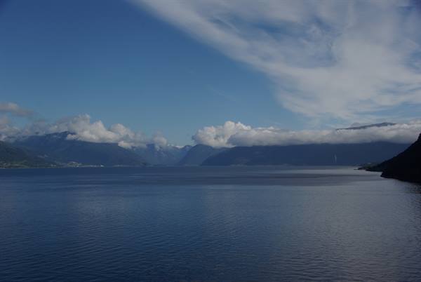 Calm fjord waters surrounded by mountains with low clouds