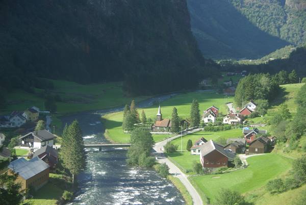 Village with red houses and church along a river between green mountains