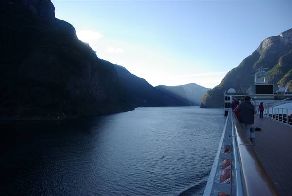 Passengers on cruise ship deck sailing between steep fjord mountains