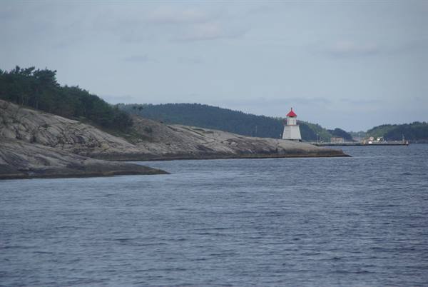 White lighthouse with red roof on granite rocks, grey water and forest