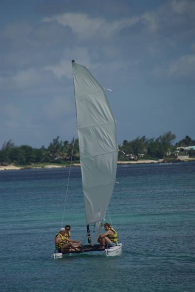 Hobby Cat sailboat with three people on turquoise sea near the beach