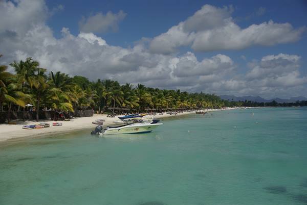 White motorboats anchored in turquoise water by a white sandy palm beach