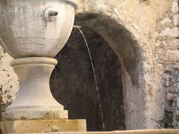 Stone fountain with water spouting in front of a medieval arch