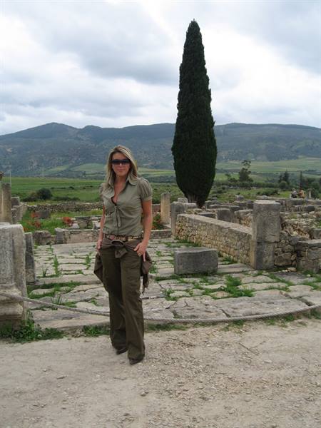 Woman in khaki among Volubilis Roman ruins, cypress and hills behind