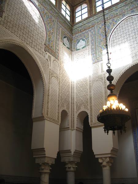 Carved plaster arches, marble columns and brass chandelier inside a medersa