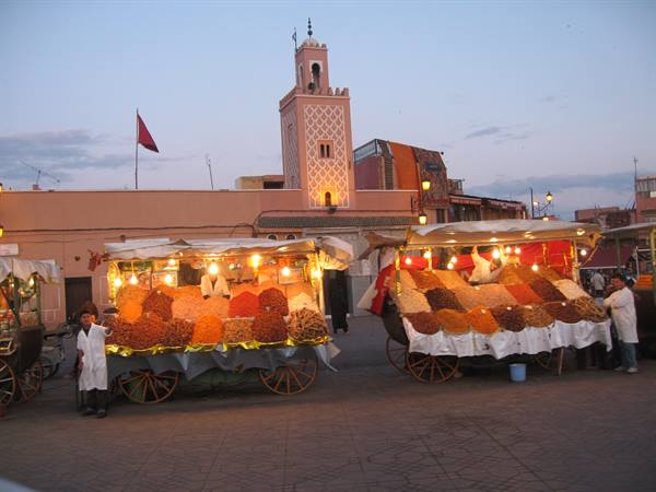 Spice carts lit up at Jemaa el-Fna, pink minaret at dusk