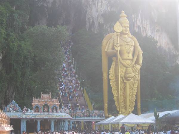 Golden Murugan statue at Batu Caves, crowds climbing the staircase
