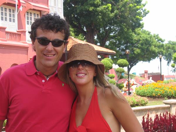 Couple in red smiling in front of Malacca's Dutch colonial buildings