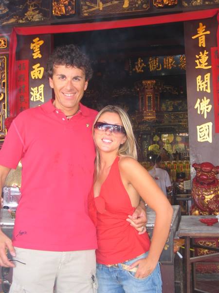 Smiling couple in red outside a Chinese temple with gold inscriptions and incense