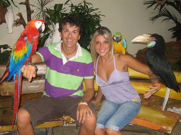 Smiling couple with macaws and hornbill on wooden bench, indoor artificial light