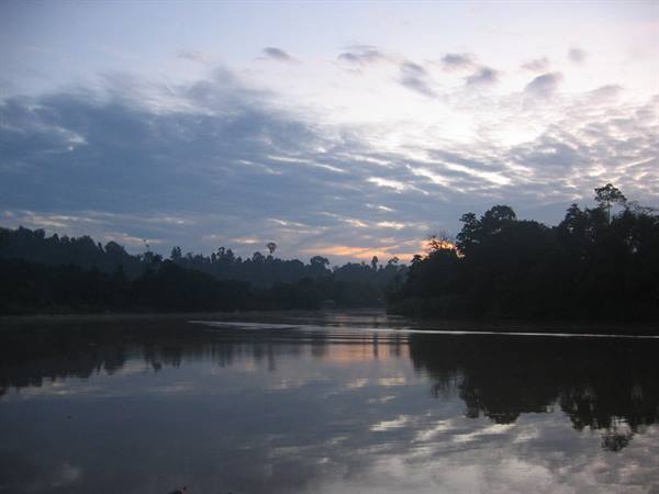 Dark river water reflects trees and clouds beneath a grey-orange sky
