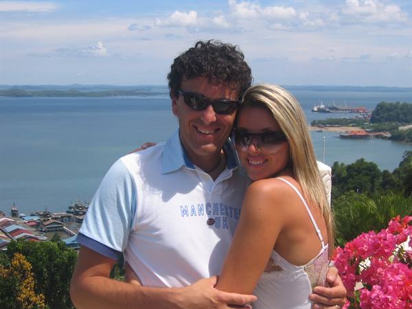 Couple in sunglasses hugging above the bay, pink flowers nearby