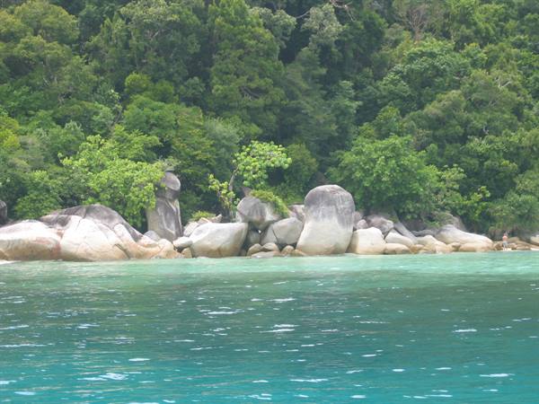 Turquoise sea in front of large granite boulders and dense tropical forest