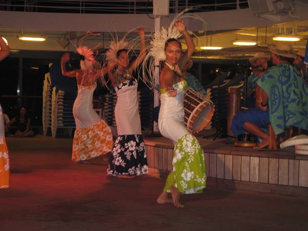 Polynesian dancers in floral skirts and straw headdresses perform at night with drums