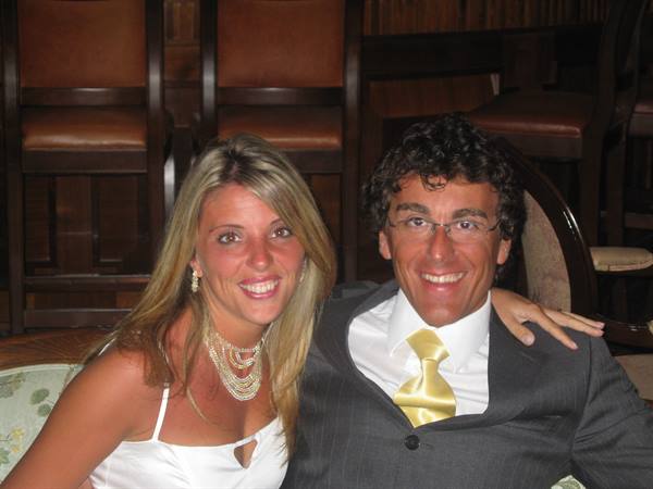 Smiling couple in elegant clothes, she wears pearl necklace, inside wooden venue