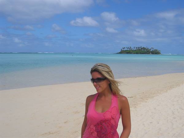 Blonde woman in pink top on white sand beach, turquoise lagoon and islet, Muri
