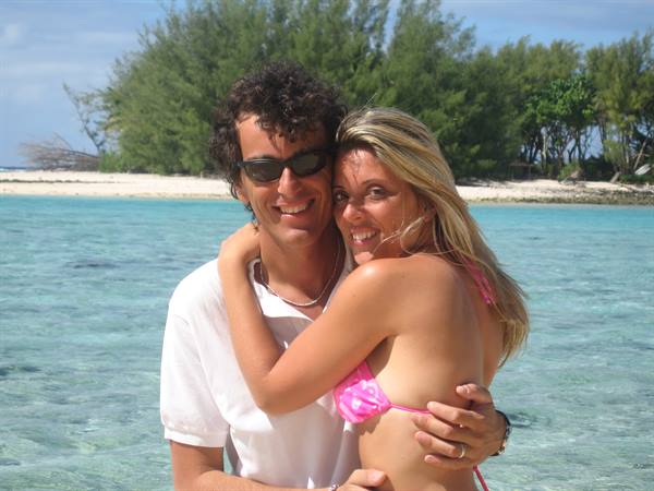 Couple embracing in turquoise water, white beach and green trees behind