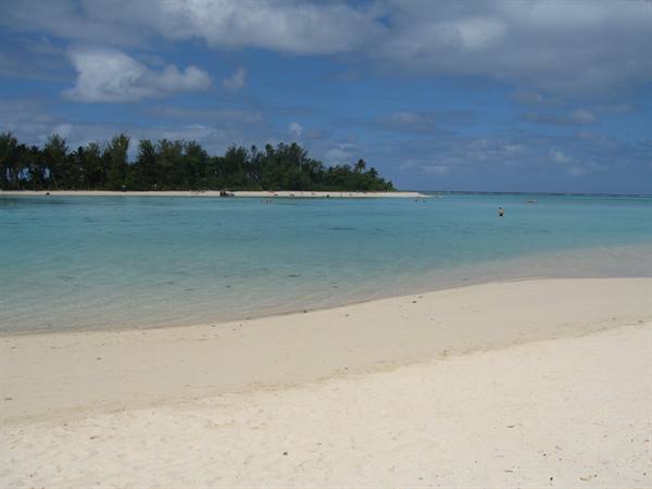 White sand beach, turquoise lagoon and palm-covered islet under clouds