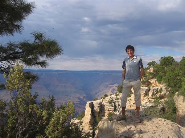 Man in blue polo standing on rock at Grand Canyon, cloudy sky