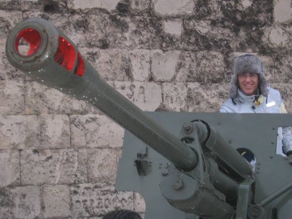 Man in fur hat posing beside a military cannon at an old fortress