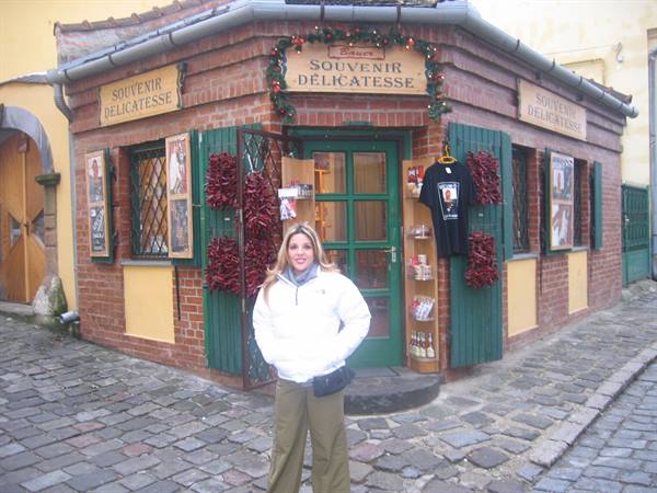Woman in white jacket in front of the brick Souvenir Delicatesse shop, cobbled street