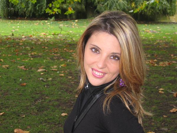 Smiling woman in black standing in a park with green grass and autumn leaves