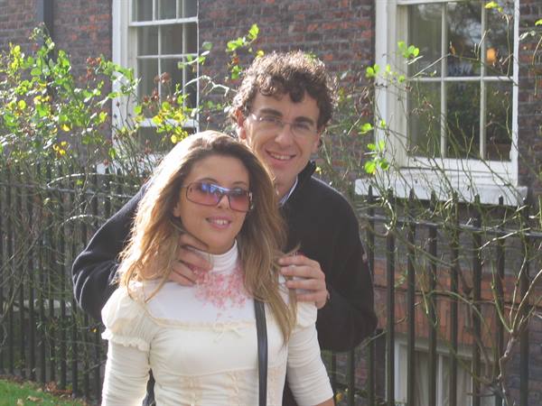 Smiling couple in front of a brick house with black iron fence and vines