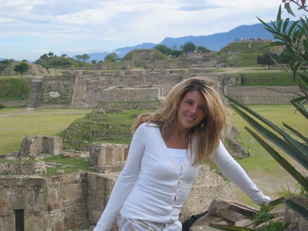 Smiling tourist on stone ruins of Monte Albán, mountains and cloudy sky