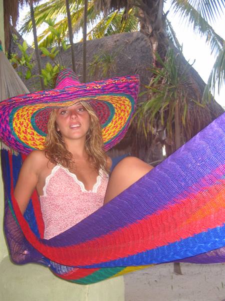Girl in colorful sombrero lounging in a striped hammock under palm trees