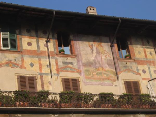 Facade with faded old frescoes, wooden shutters and a rose balcony