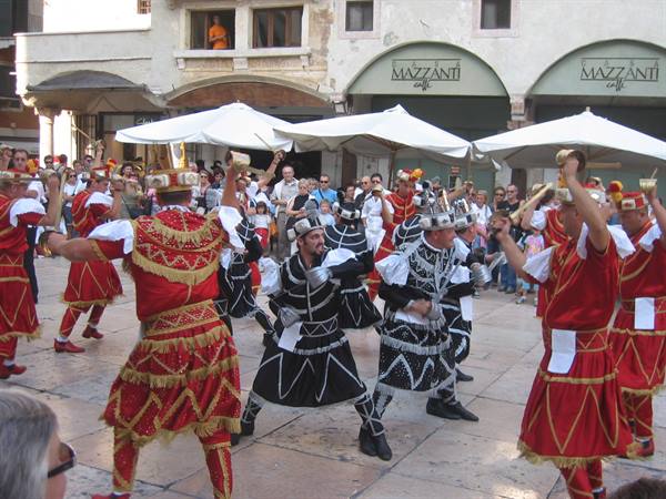 Dancers in red and black costumes with cowbells perform in a town square
