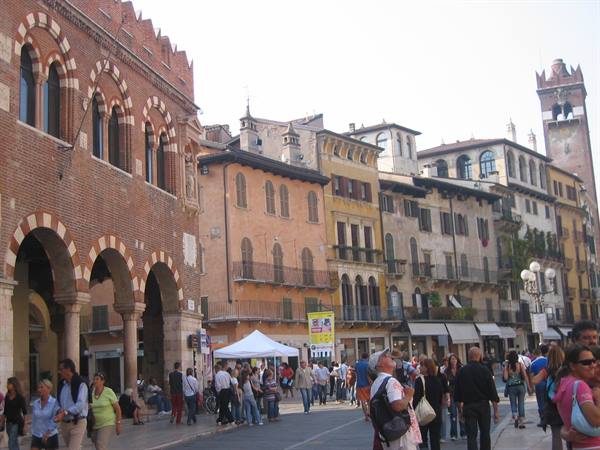 Tourists stroll past colored houses and brick palace in Verona