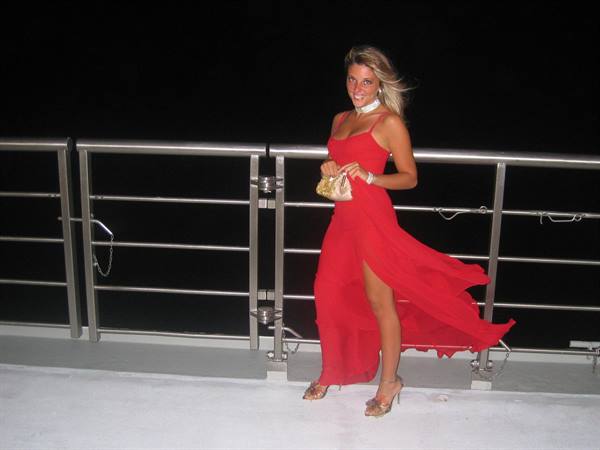 Woman in long red dress with gold purse, at night on deck with metal railing