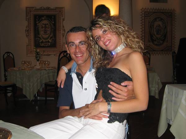 Couple hugging at a restaurant, she wears black top and necklace, set tables
