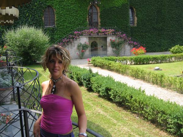 Woman in pink top in front of ivy-covered villa with flowered staircase