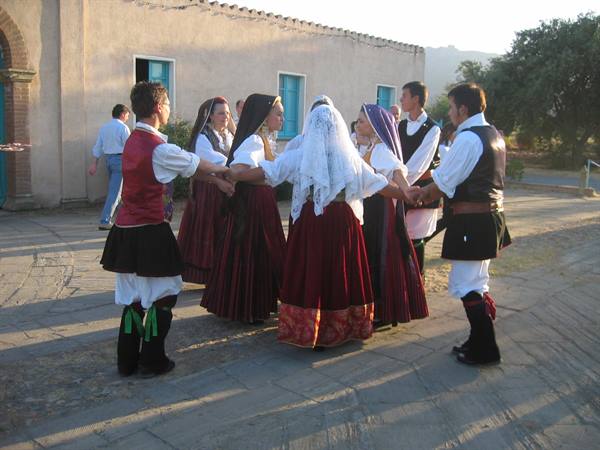 Dancers in traditional Sardinian costumes hold hands in a circle at golden hour